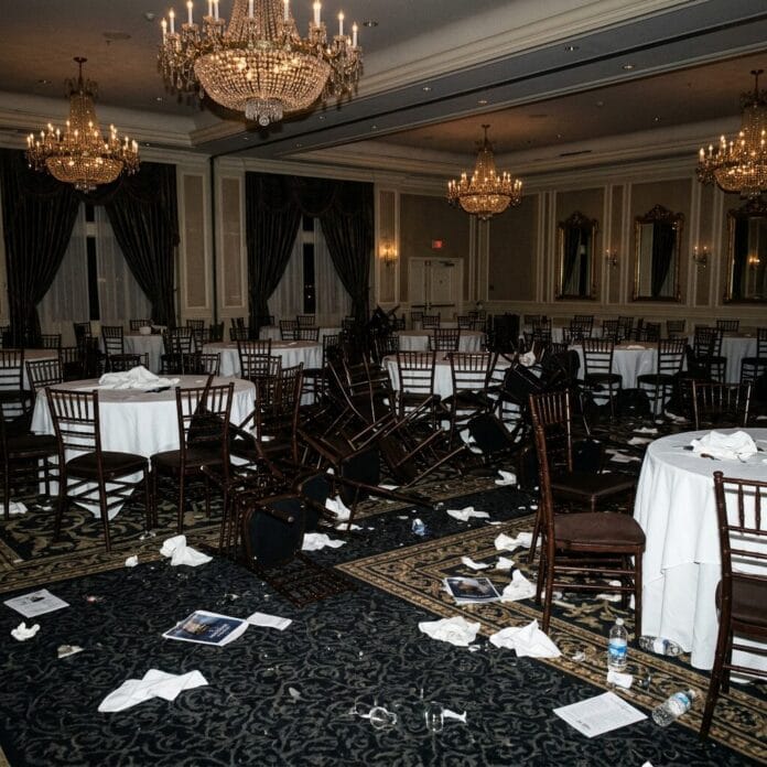 Banquet hall with overturned chairs, scattered papers, and trash on the floor