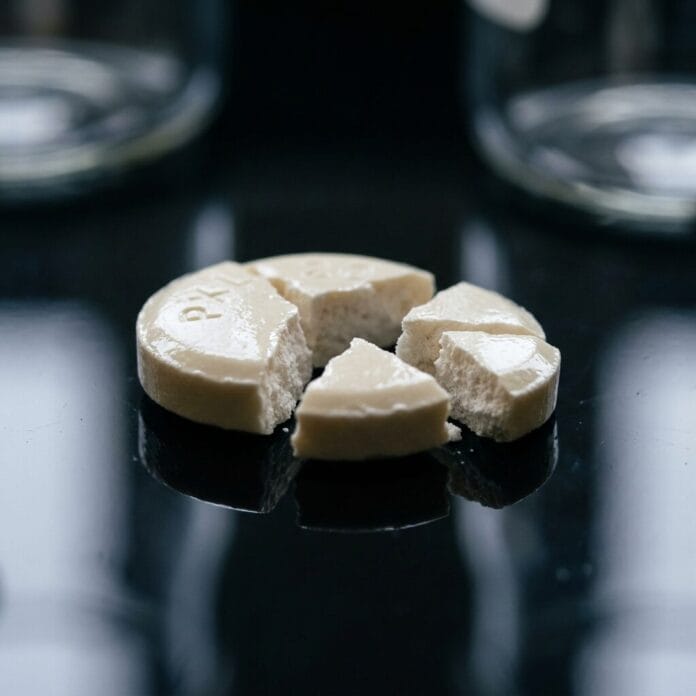 Broken white round tablet split into four pieces on a black shiny surface.