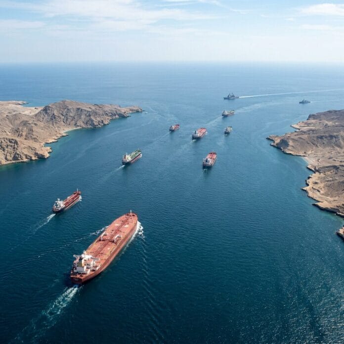 Cargo ships and naval vessels sailing through a narrow strait with rocky coasts