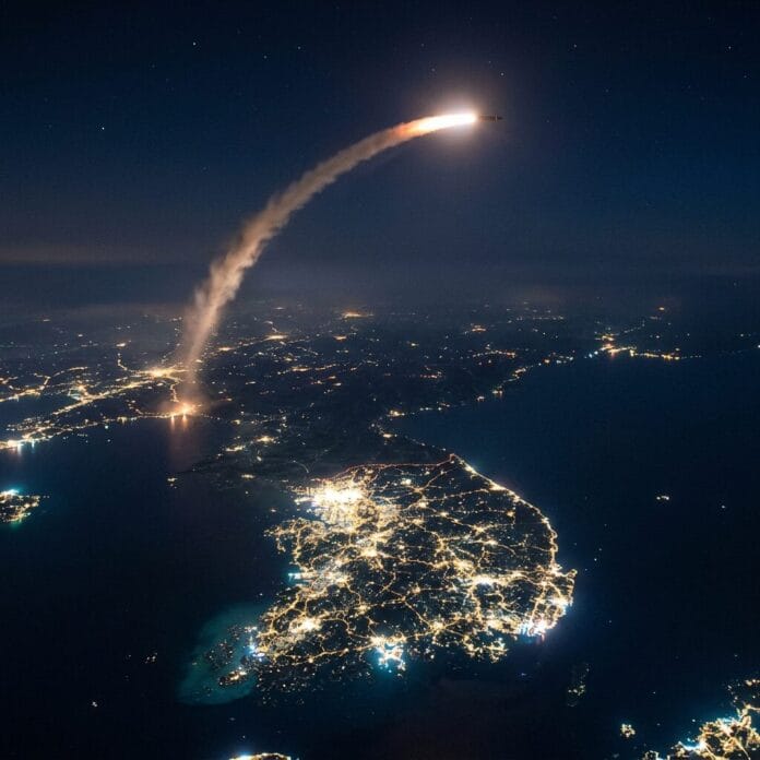Missile launching with bright trail over illuminated landmass and city lights at night