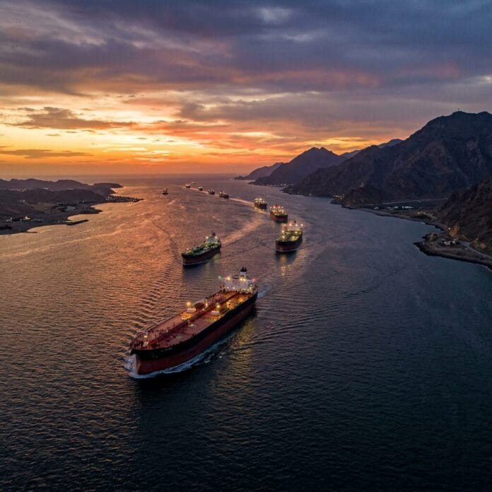 Multiple oil tankers sailing in a narrow waterway at sunset with mountains on one side