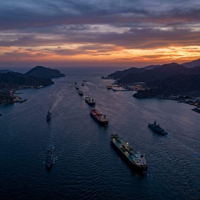 Several oil tankers sailing through a mountainous strait at sunset with calm waters
