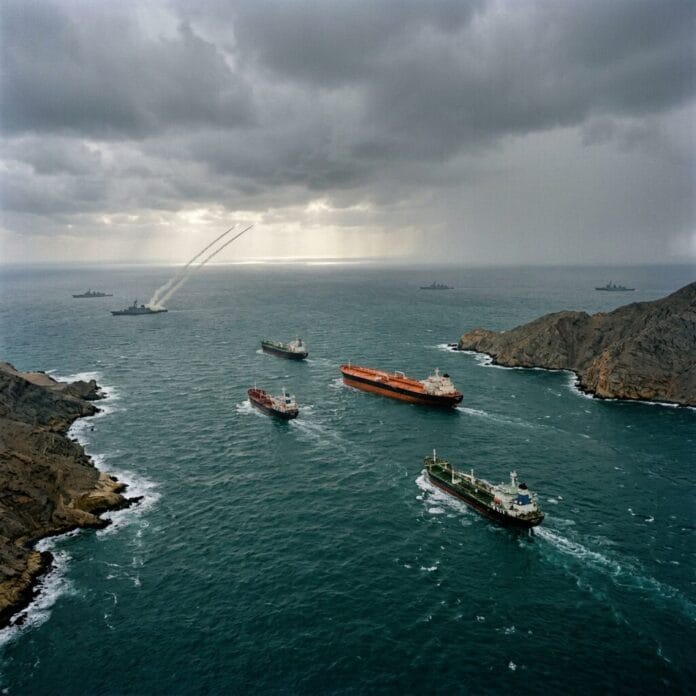 Cargo ships sailing through a narrow sea with military ships launching missiles nearby under a cloudy sky